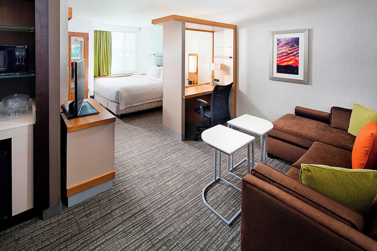 Una habitación de hotel con cama, escritorio con computadora, una zona de estar pequeña y televisión.