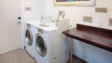 Un área de lavandería con dos lavadoras, un letrero de almacenamiento de ropa blanca y un cartel con los tiempos de lavado.