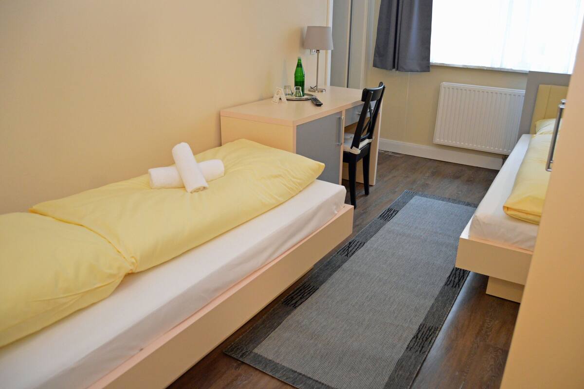 Ein kleines Zimmer mit einem Einzelbett, einem Schreibtisch, einem Stuhl und einer Heizung.