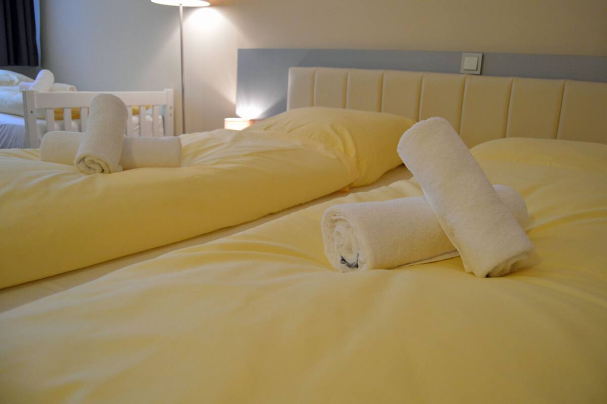 Ein Hotelzimmer mit zwei Betten, jeweils mit einem ordentlich gerollten weißen Handtuch und einer Kopfteil.