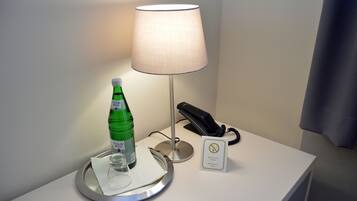 Een hotelkamer met een nachtkastje met een lamp, telefoon, een fles water en een glas.
