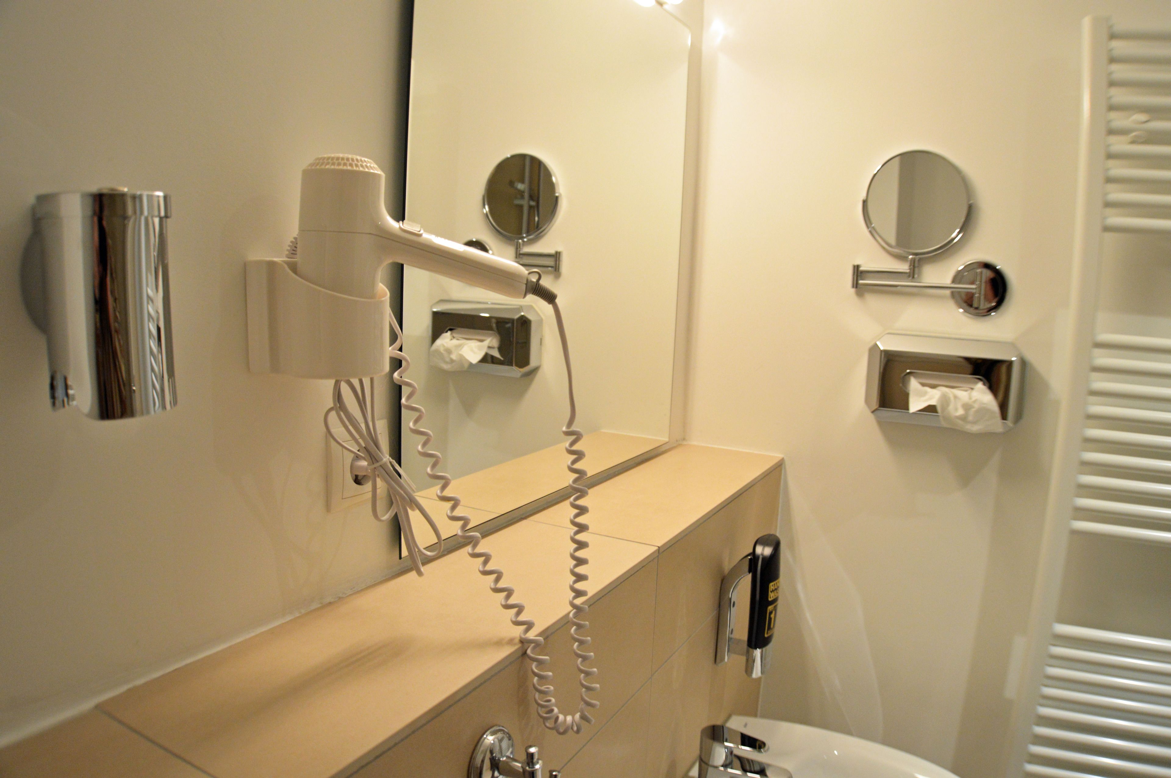 A bathroom with a hairdryer, a mirror, a towel dispenser, and a toilet.