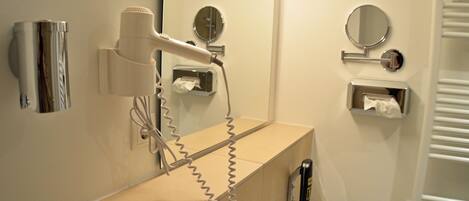 A bathroom with a hairdryer, a mirror, a towel dispenser, and a toilet.