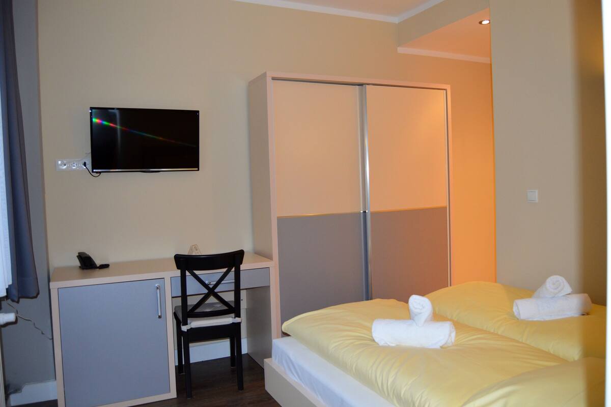 Ein Hotelzimmer mit einem Bett, einem Schreibtisch mit Stuhl, einem an der Wand befestigten Fernseher und einem Kleiderschrank.