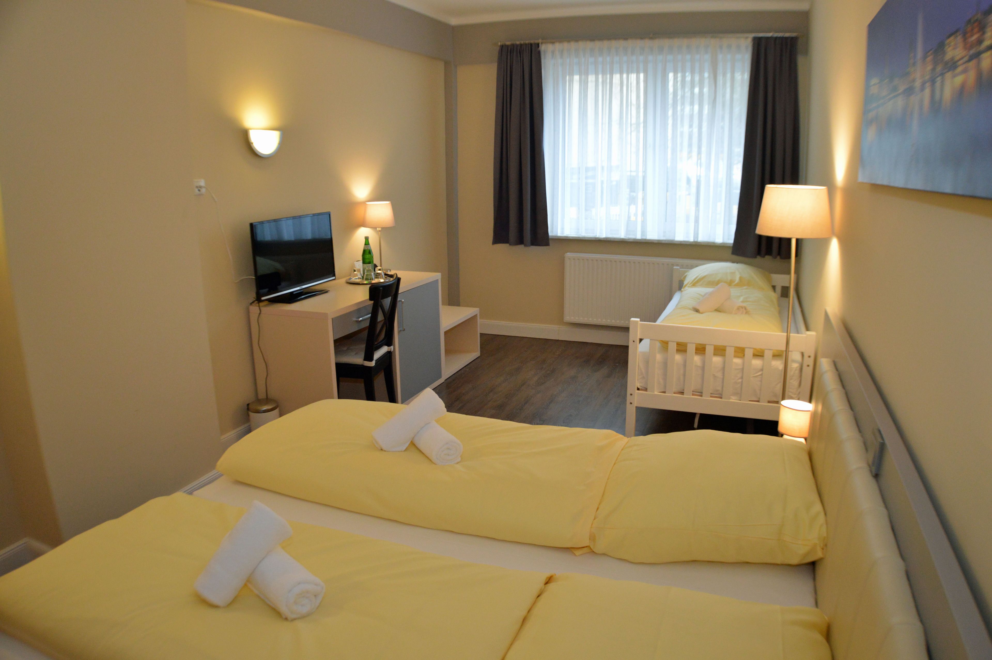 Een hotelkamer met twee bedden, een bureau, een televisie en een raam met gordijnen.