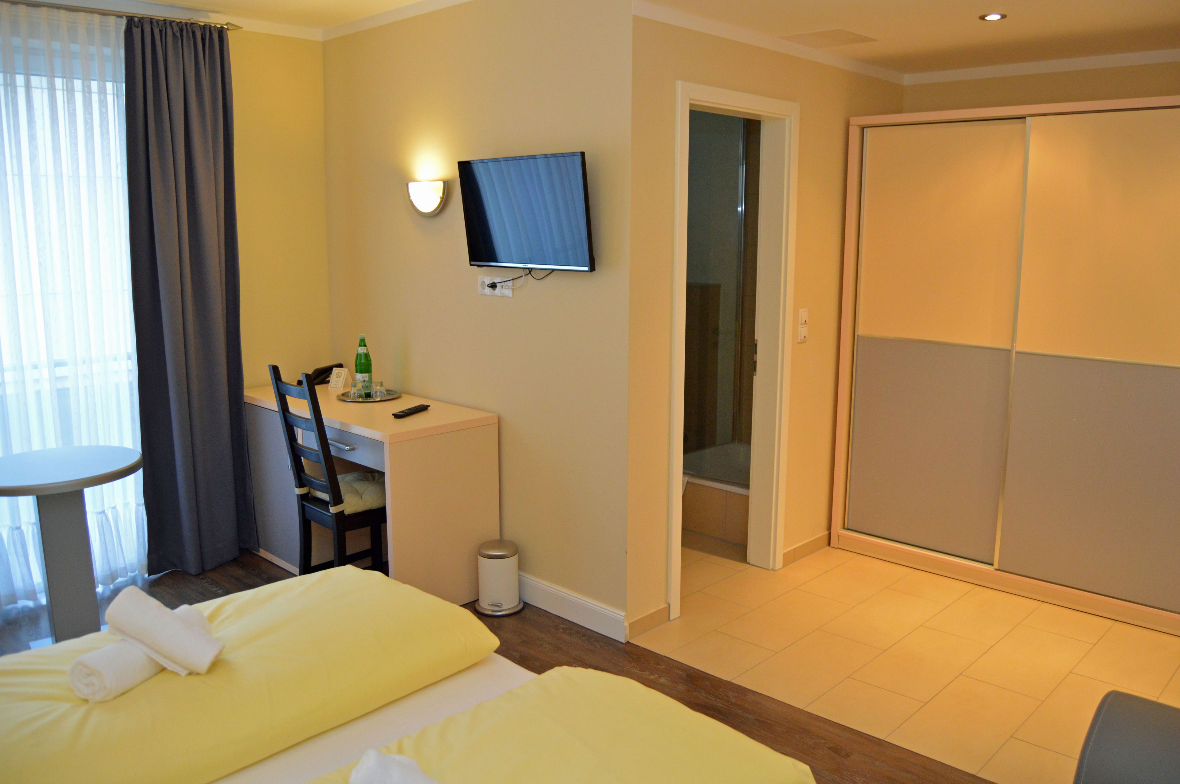 A hotel room with two beds, a desk with a chair, a TV, and a sliding door closet.