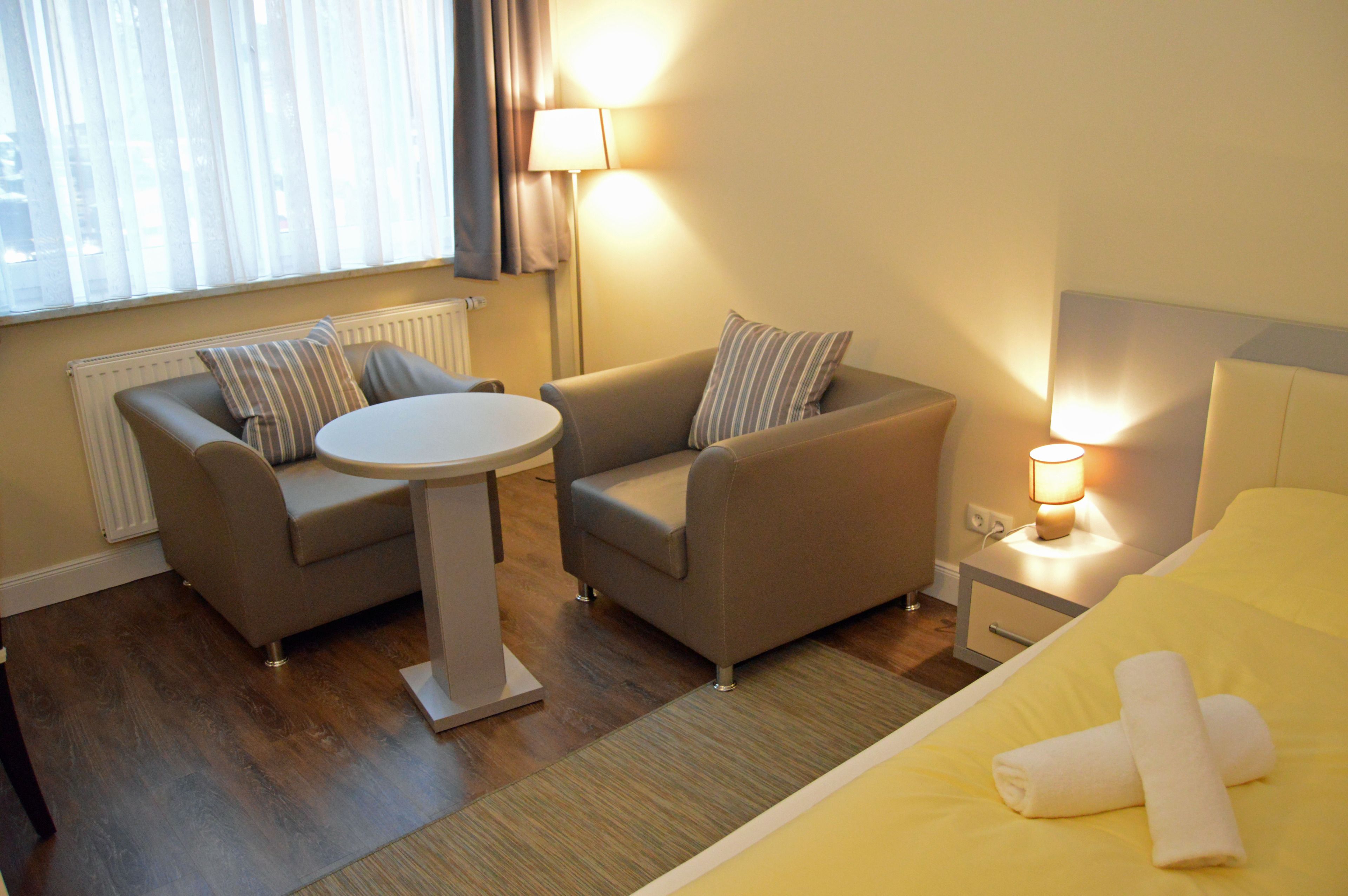 A hotel room with a bed, two sofas, a small table, and a nightstand with a lamp.