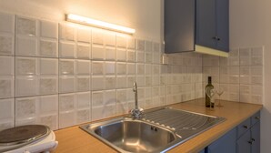 A kitchen with a stainless steel sink, a light under the countertop, and a bottle of olive oil on the counter. - Pansion Mary Studios (Zakynthos)
