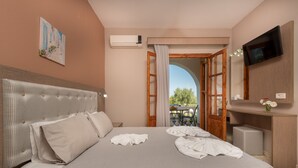 A hotel room with a large bed, a flat-screen TV, an air conditioning unit, and a view of the outdoors through an open door. - Pansion Mary Studios (Zakynthos)