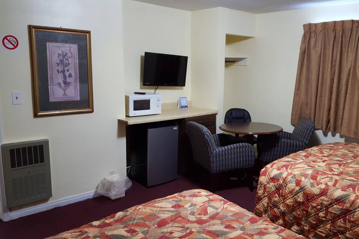 A hotel room with two beds, a desk with a TV, a microwave, and a chair.