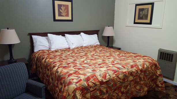 A hotel room with a large bed, two bedside lamps, a chair, and two framed pictures on the wall. - Colonial West Motel (Batavia)