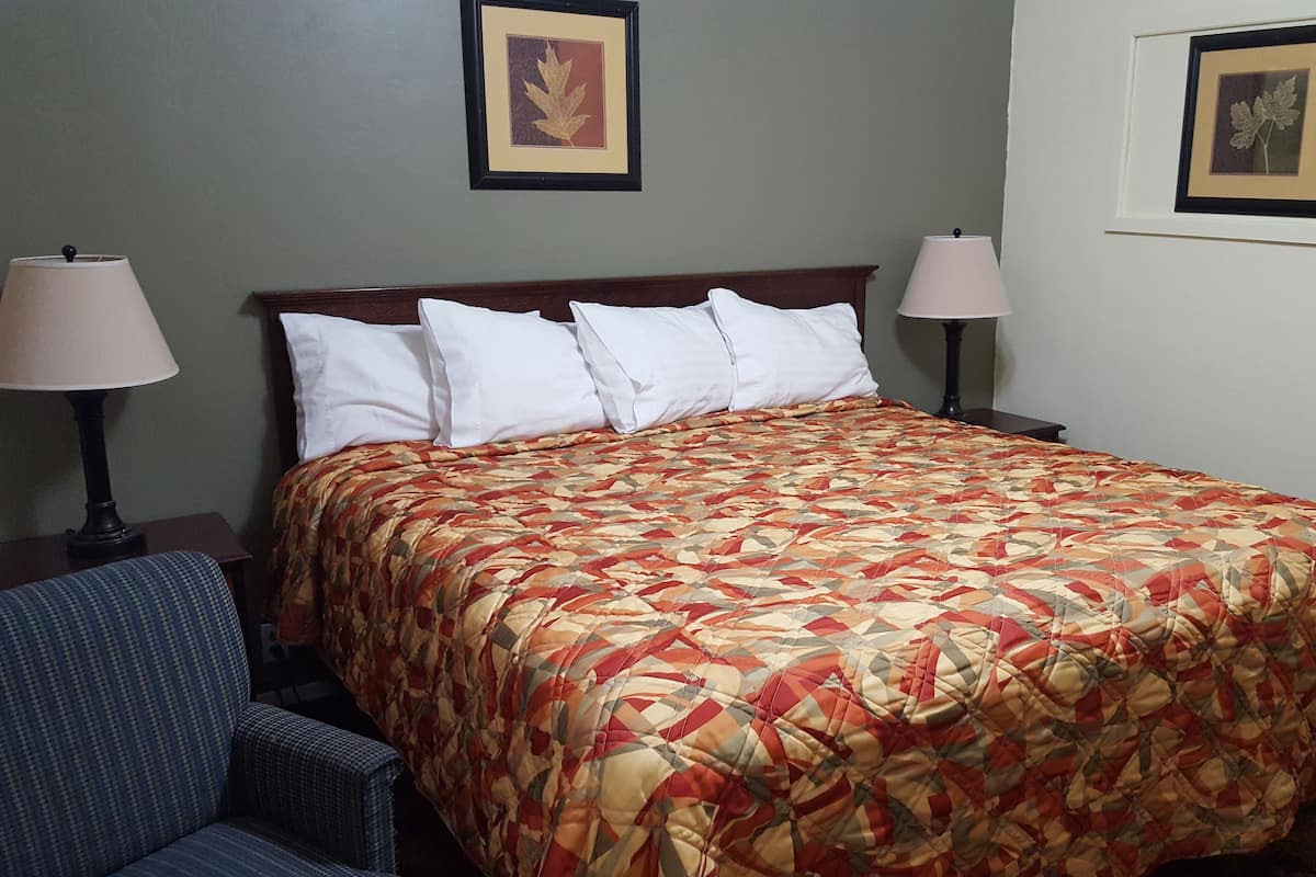 A hotel room with a large bed, two bedside lamps, a chair, and two framed pictures on the wall.