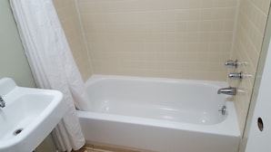 A bathroom with a bathtub, a sink, and a shower curtain. - Colonial West Motel (Batavia)
