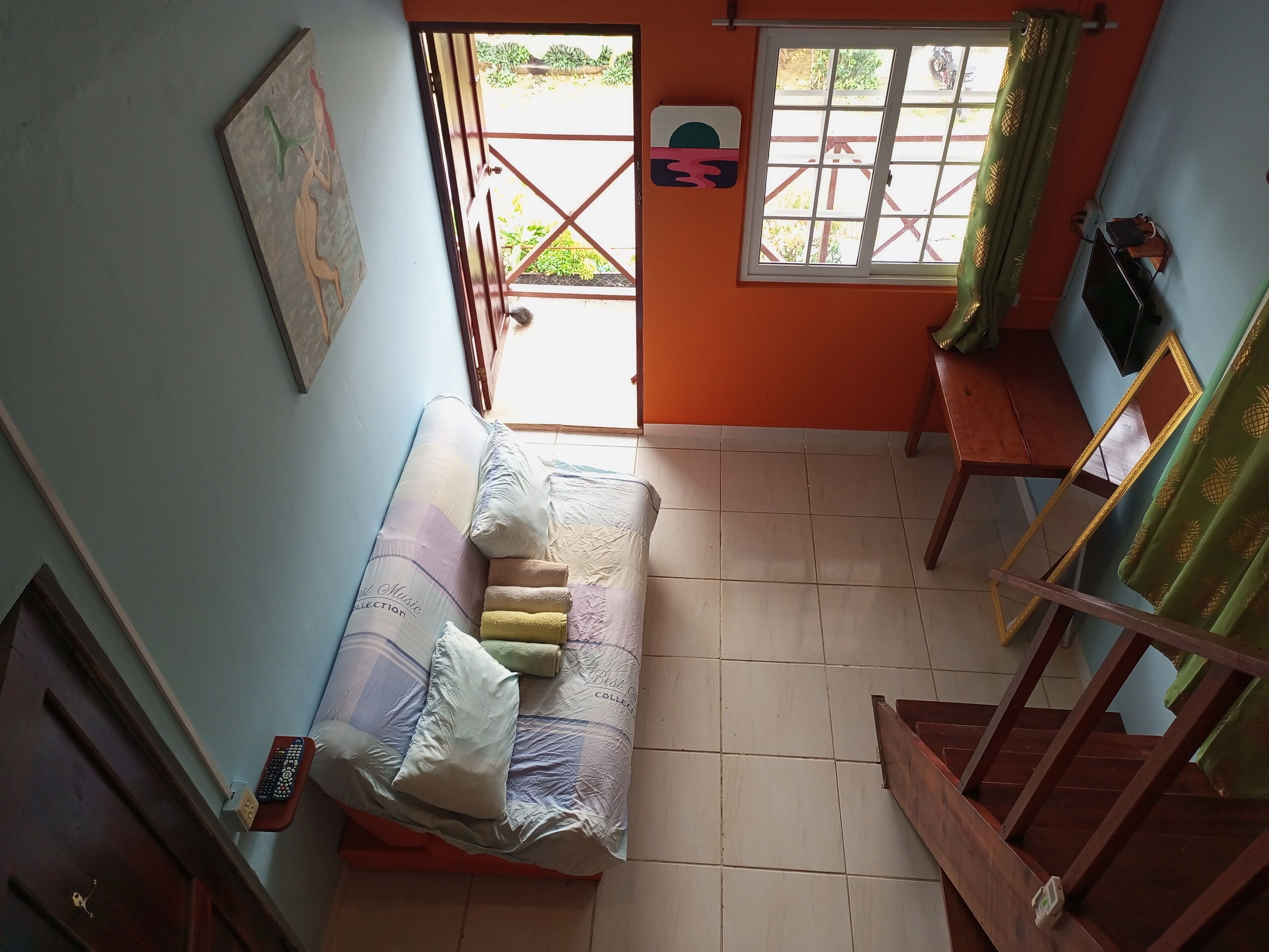 Una habitación con cama, televisión, ventana con cortinas, puerta y una escalera.