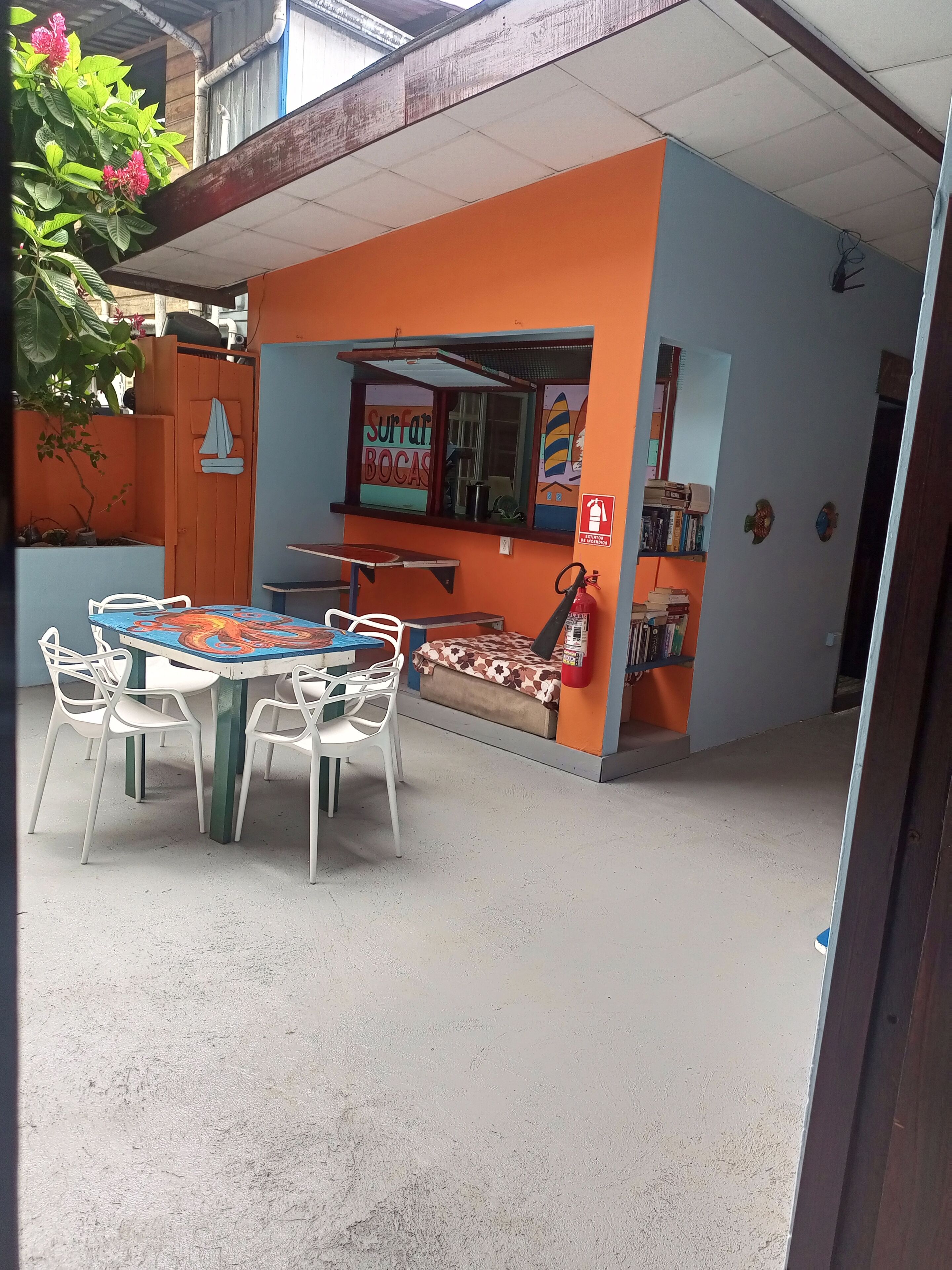 An outdoor seating area with a table and chairs, a small window with a sailboat decoration, and a fire extinguisher on the wall.