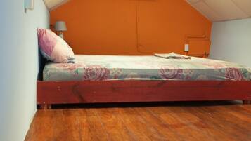 Un dormitorio con techo inclinado, una cama individual con ropa de cama floral, un equipo de aire acondicionado y piso de madera.