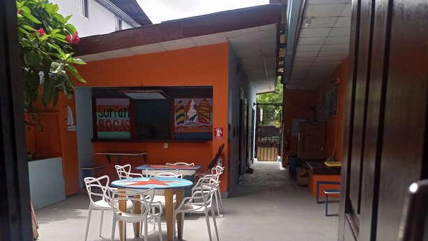 Un área de comedor al aire libre con una mesa redonda y sillas blancas, rodeada de paredes naranjas y un techo azul.
