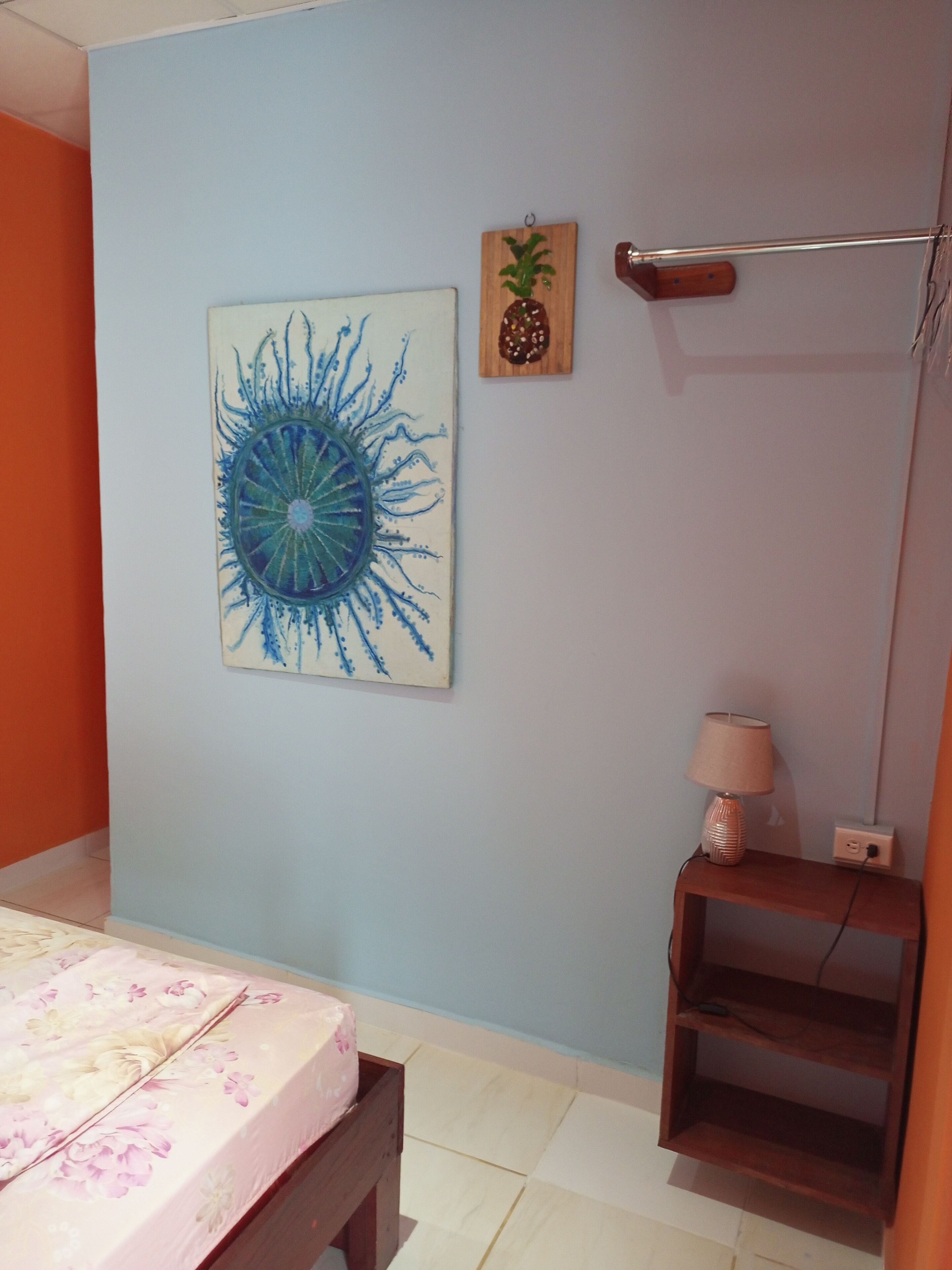 Een slaapkamer met een bed, een kunstwerk aan de muur, een klein plankje en een lamp.