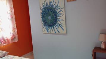 Una camera da letto con un letto, un condizionatore d'aria a muro, una ventola a soffitto, un quadro incorniciato, una piccola pianta in vaso e un comodino con una lampada.
