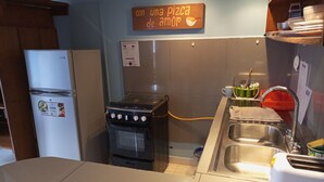 Una cocina compacta con estufa a gas, refrigerador, lavamanos y tostadora. Un letrero en la pared dice "con una pizza de amor".