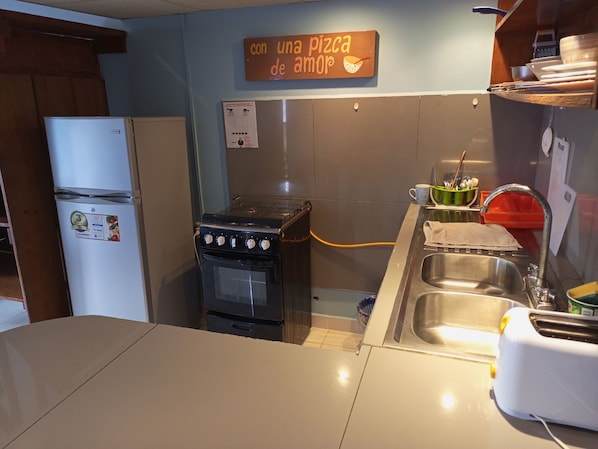 Eine kompakte Küche mit Gaskochfeld, Kühlschrank, Spüle und Toaster. Ein Schild an der Wand zeigt die Aufschrift 'con una pizza de amor'.