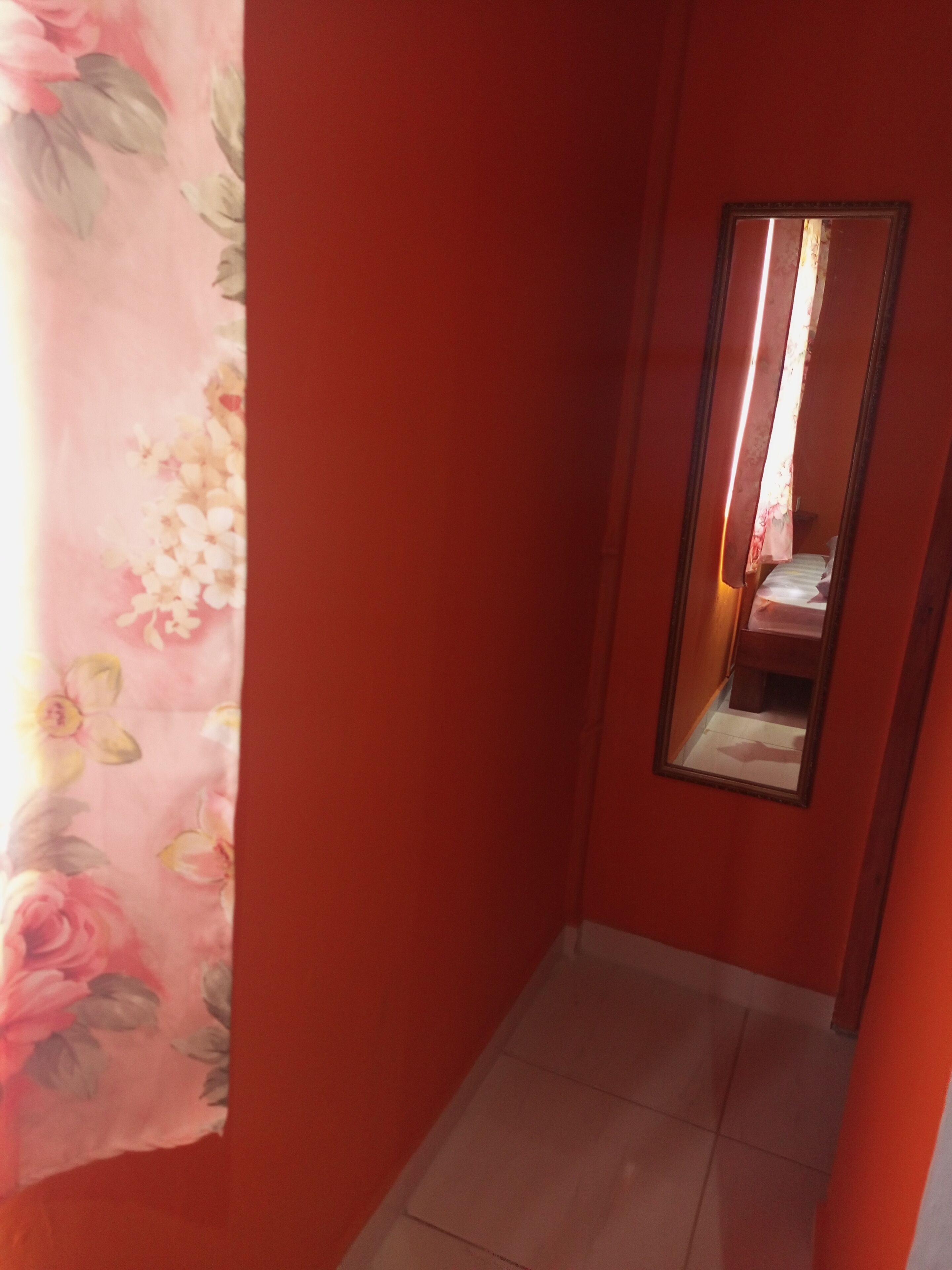 A narrow hallway with a floral curtain on one side and a mirror on the wall.