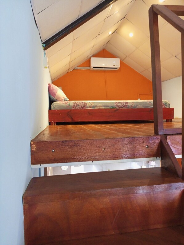 A bedroom with a sloped ceiling, a bed, and a wooden staircase. - Surfari Bocas (Bocas del Toro)