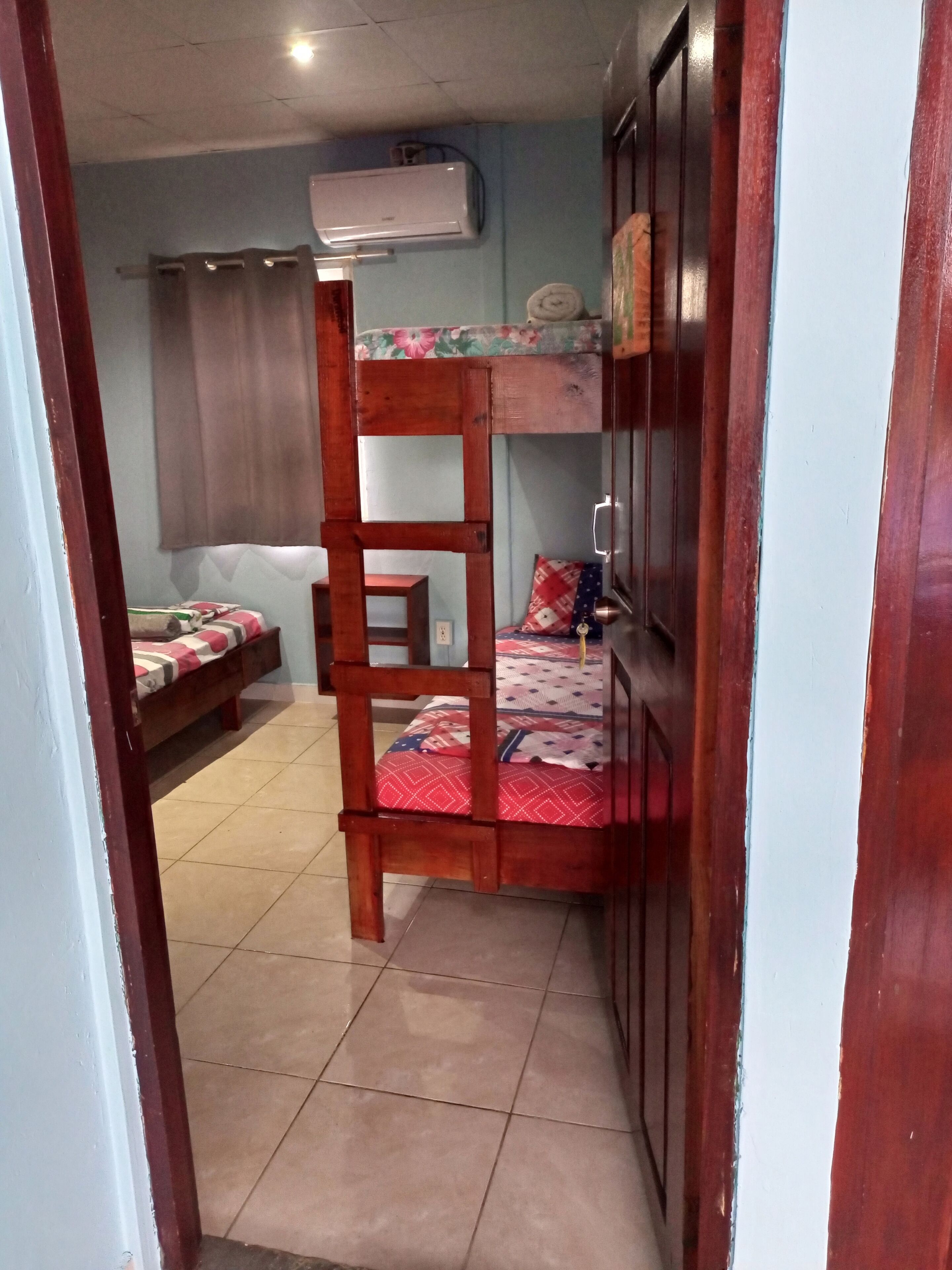 A room with a bunk bed, a small table, a chair, a sofa, and an air conditioning unit.