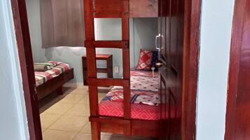 A room with a bunk bed, a small table, a chair, a sofa, and an air conditioning unit.