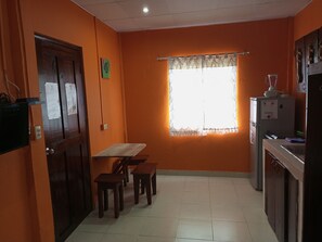 A kitchen with a wooden table and stools, a window with a lace curtain, and a refrigerator. - Surfari Bocas (Bocas del Toro)