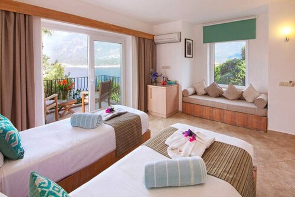 Camera d'albergo con due letti, un balcone, un'area salotto con cuscini e vista sull'esterno.
