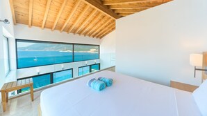 Un dormitorio con una cama grande, techo de madera y un balcón con vista al mar.