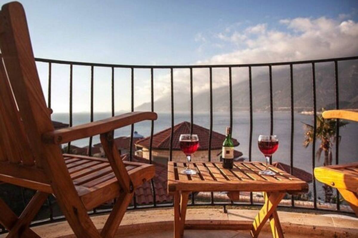 Una sedia e un tavolo di legno su un balcone con vista sul mare e sulle montagne.