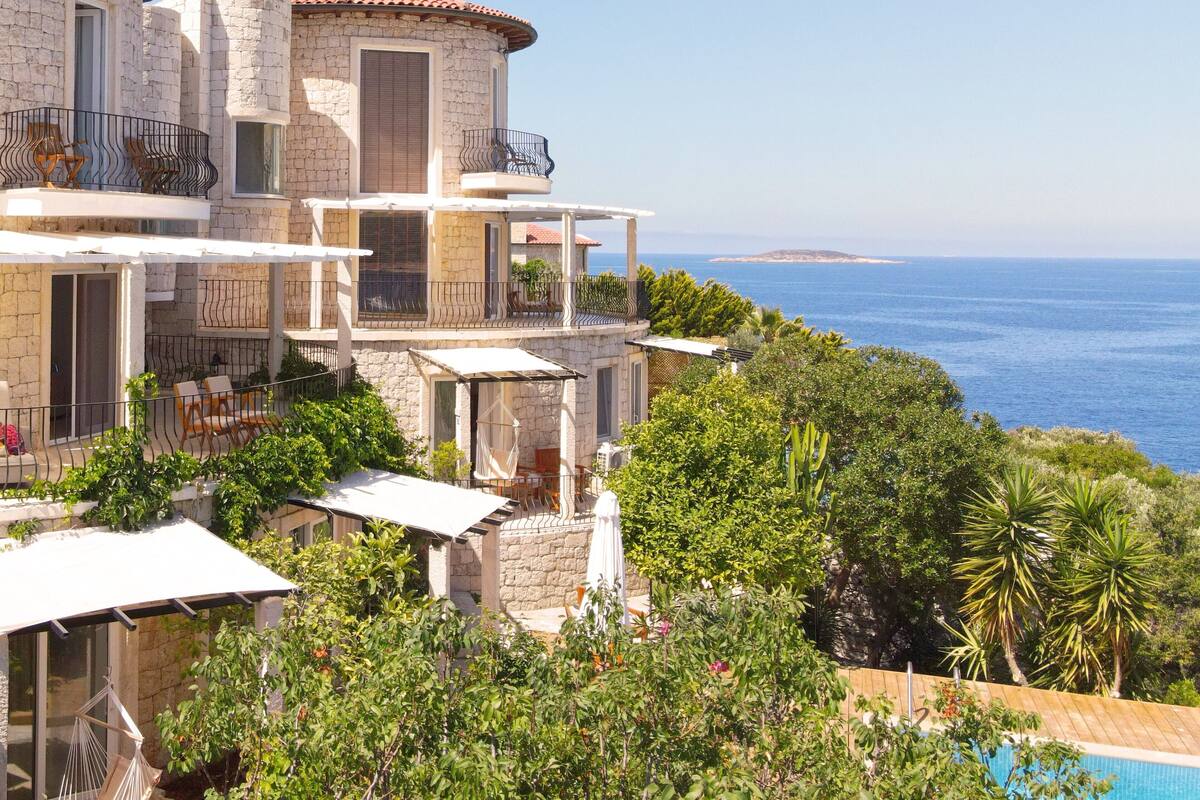 Un edificio in pietra a più piani con balconi, una piscina e vista sul mare.