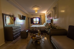 Habitación de hotel con cama, sofá, cómoda, espejo, candelabro y ventana con cortinas.