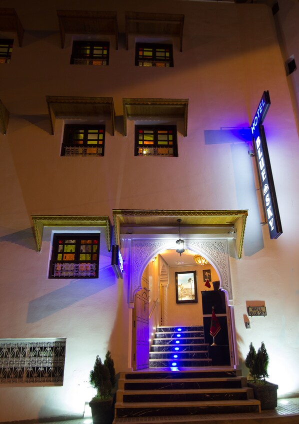 A hotel entrance with a staircase, a neon sign, and a flag.