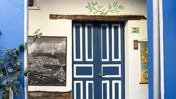 A blue door with white decorative panels, a small window with a map, and a potted plant on the ground. - Blue Door Housing Historic Quito (Quito)