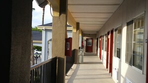 Un couloir avec une passerelle couverte, des portes rouges et un extincteur fixé au mur.