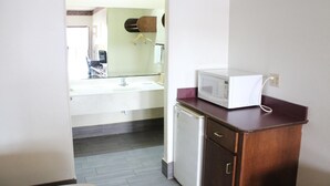 Une cuisine compacte avec un four à micro-ondes posé sur un plan de travail en bois, un petit réfrigérateur et un évier surmonté d’un miroir.