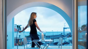 A woman standing by a window with a candle on a table, overlooking a marina with boats and a bridge. - Palazzo Murrano adults only (Vico Equense)