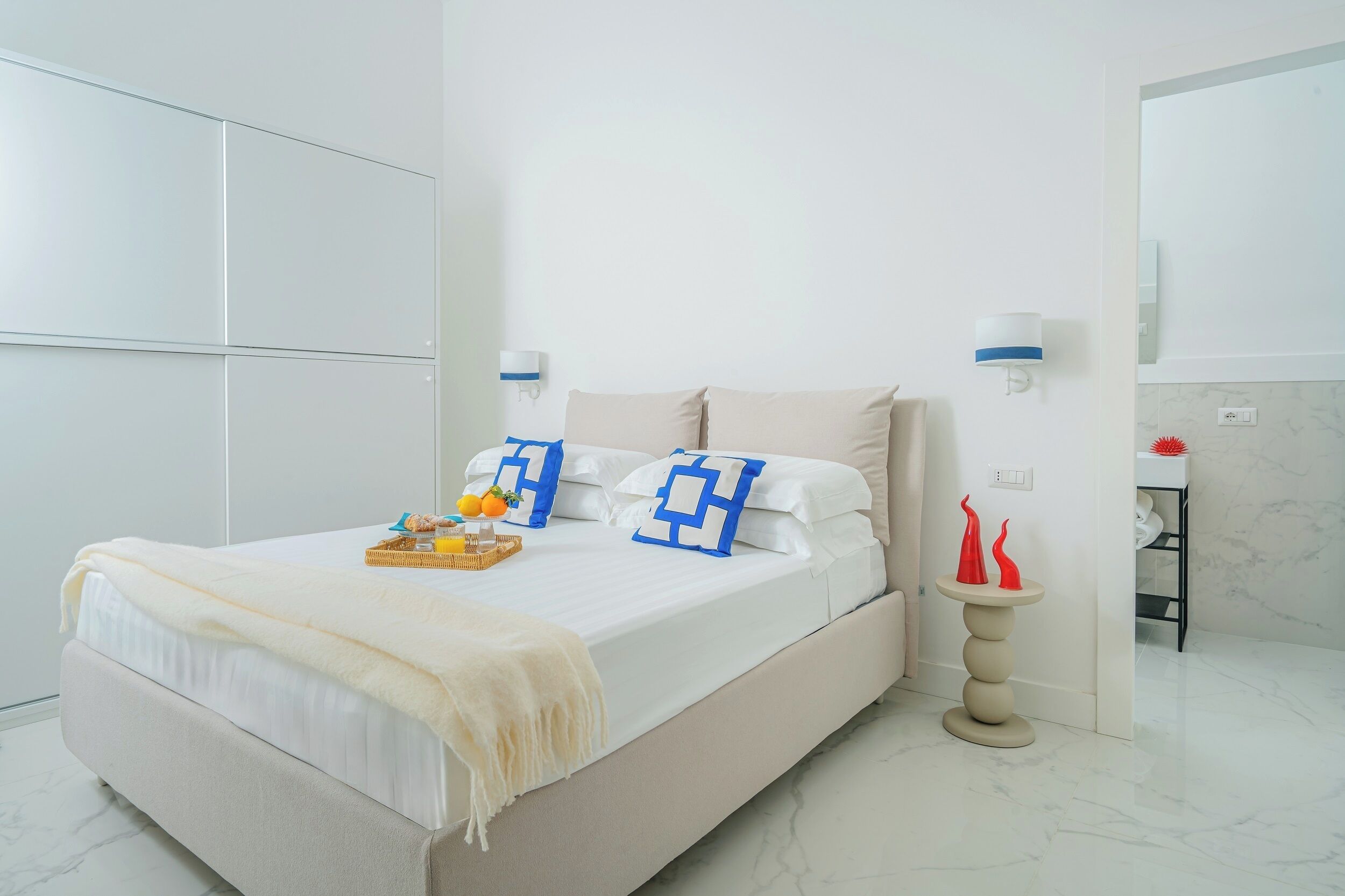 Une chambre à coucher moderne, avec un lit, des tables de chevet et une petite table agrémentée d’objets décoratifs.