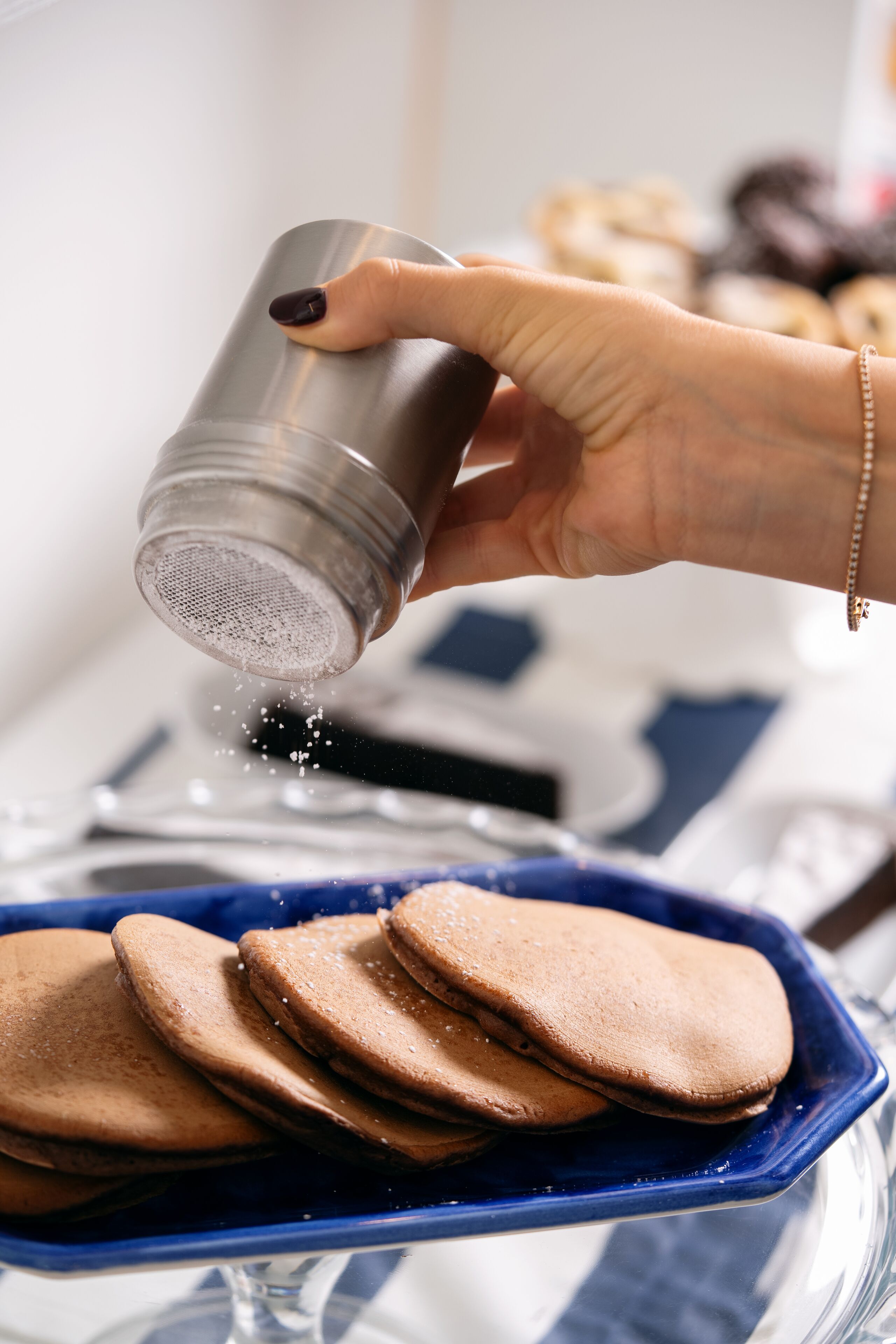 A hand sprinkling salt over cookies in a blue dish.