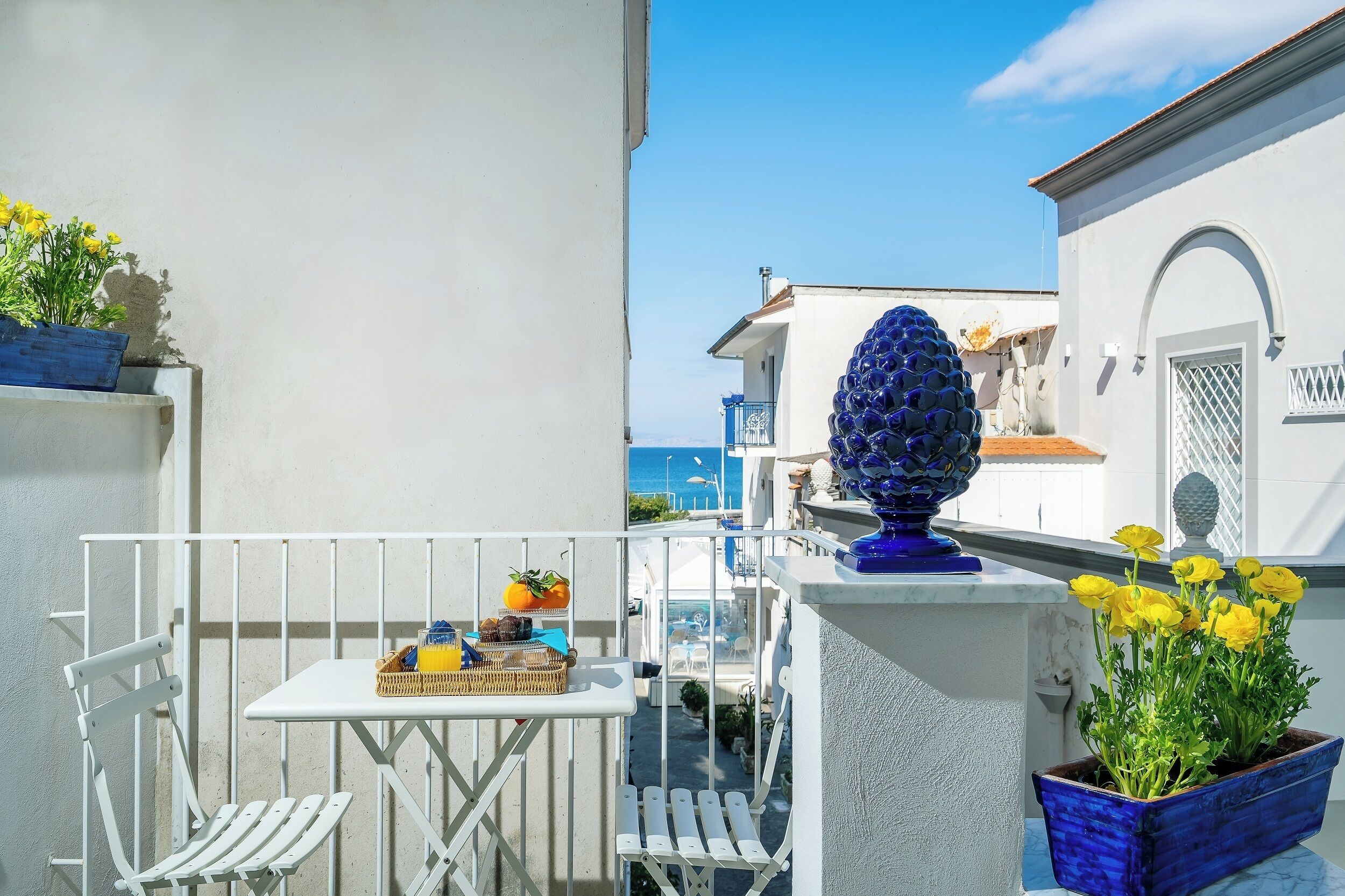 Un balcon avec une table blanche, des chaises et un pot de fleurs contenant des fleurs jaunes.