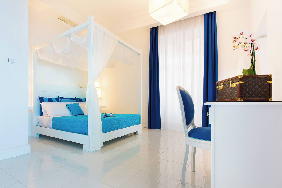 A bedroom with a four-poster bed, a desk with a chair, and a vase of flowers.