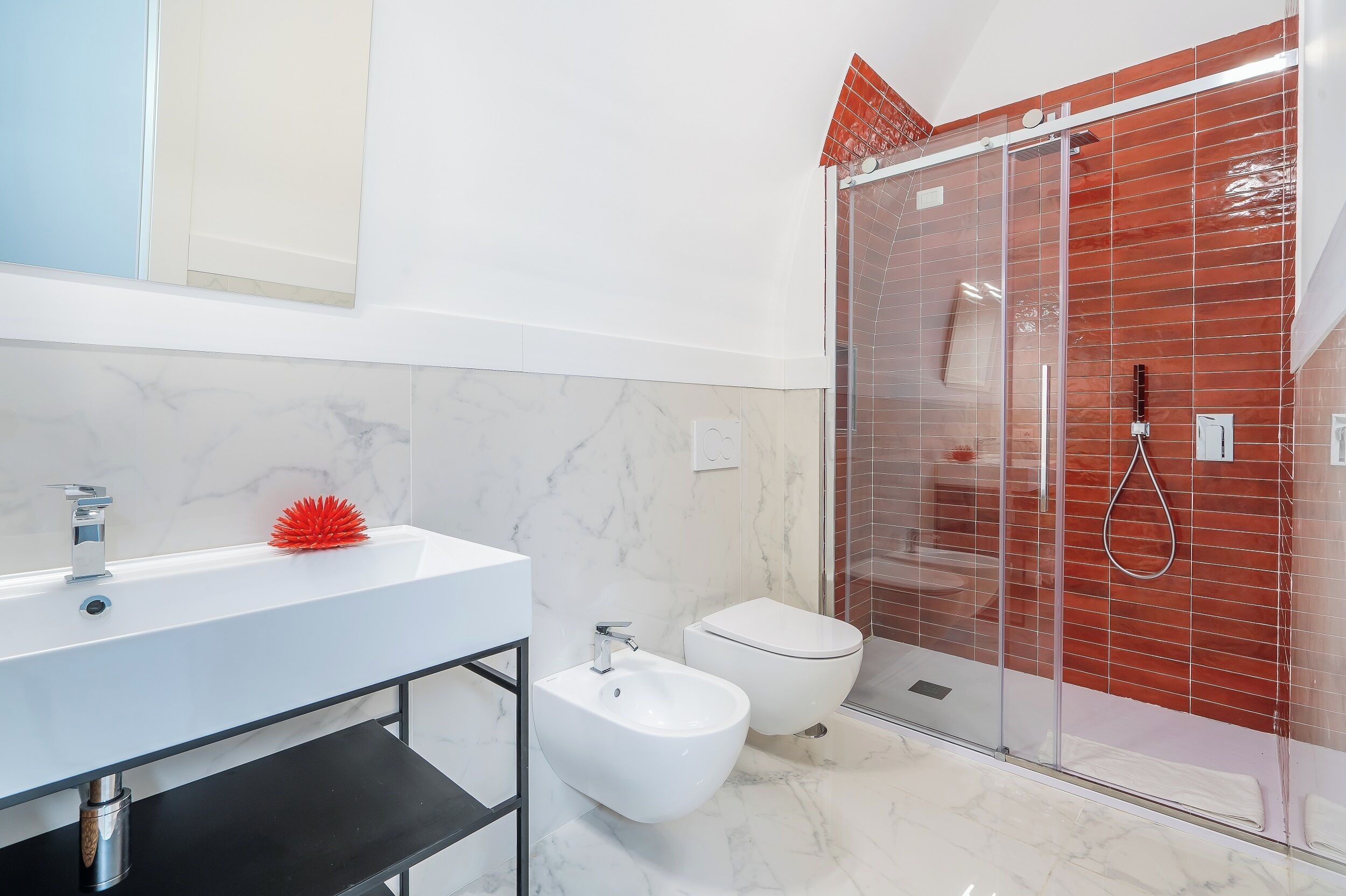 A modern bathroom with a white sink, bidet, and glass-enclosed shower.