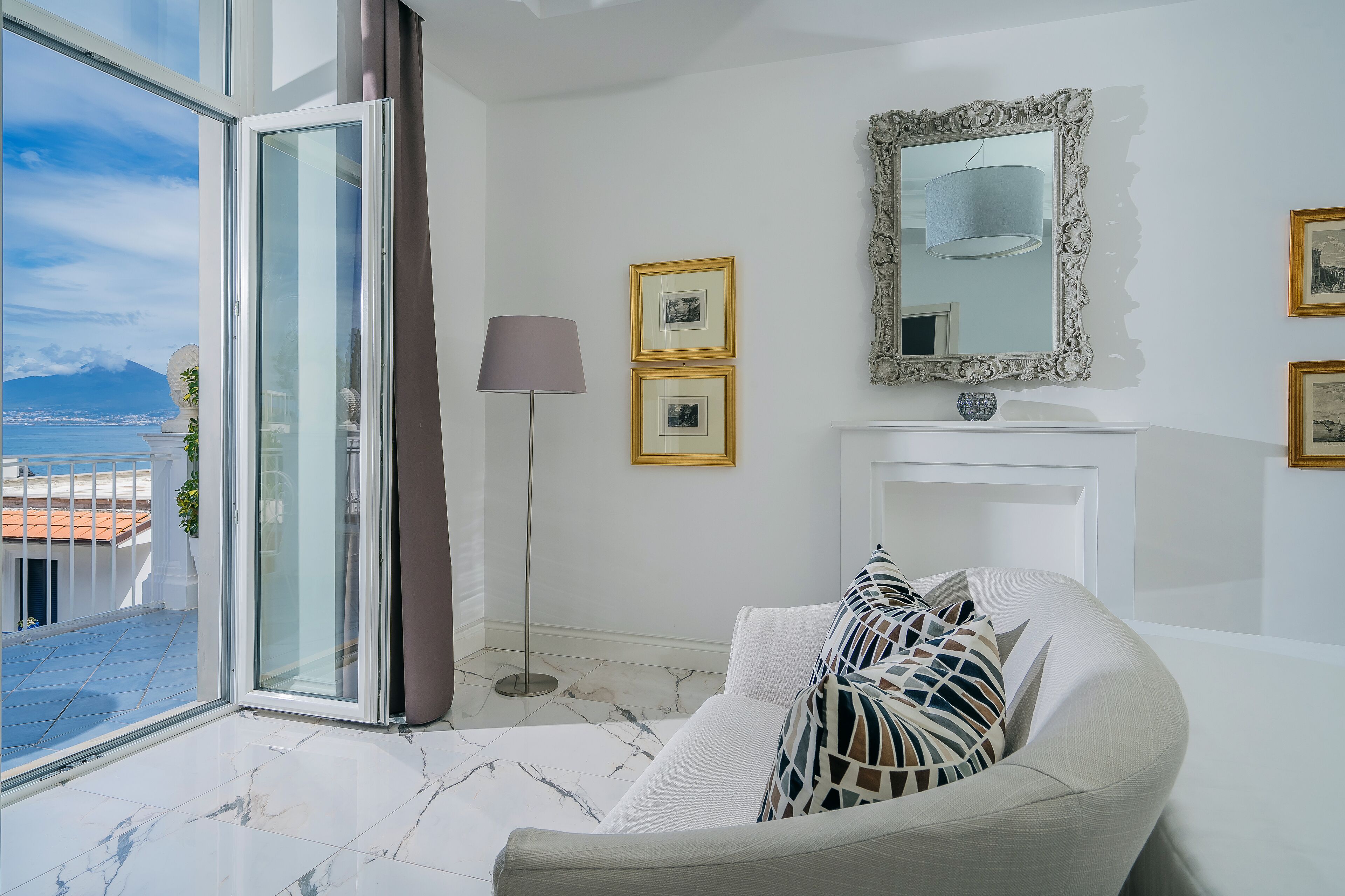 A modern living room with a large window, a white sofa, a floor lamp, and a fireplace.