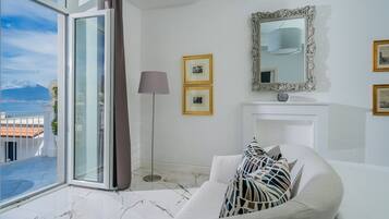 A modern living room with a large window, a white sofa, a floor lamp, and a fireplace.