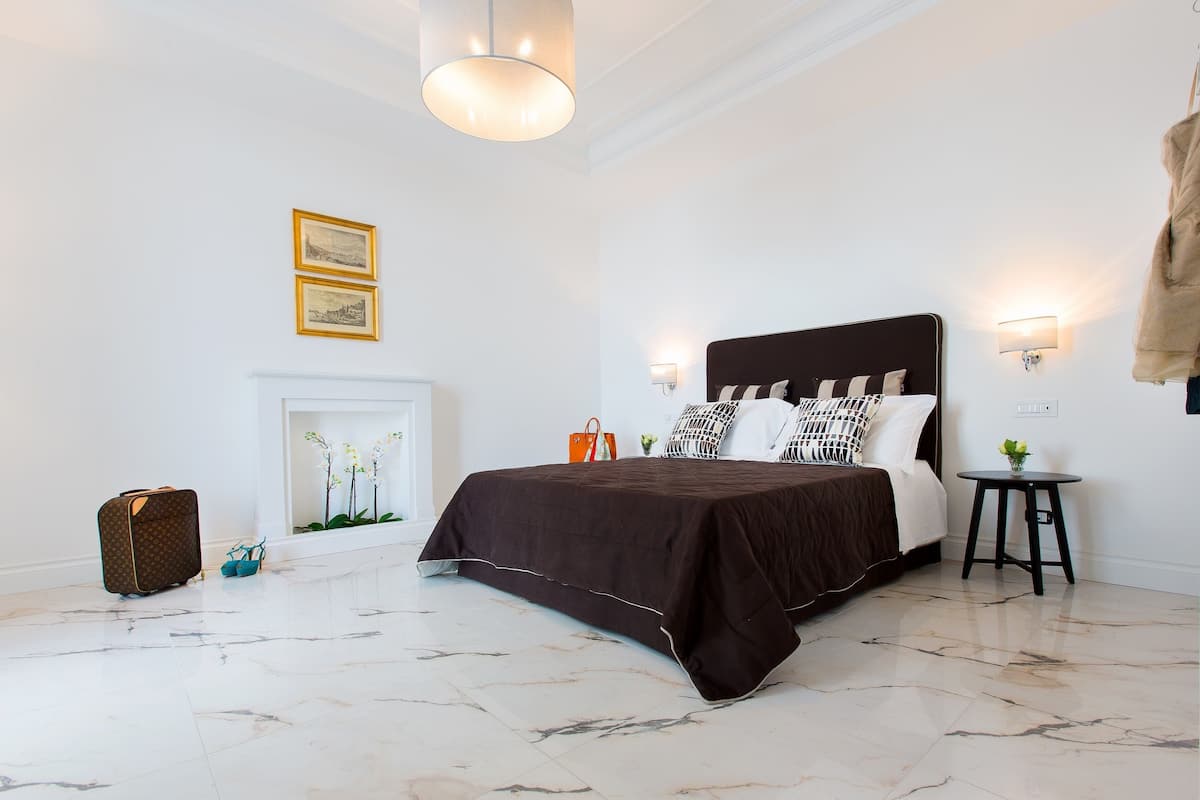 A bedroom with a large bed, a fireplace, and a suitcase on the floor.