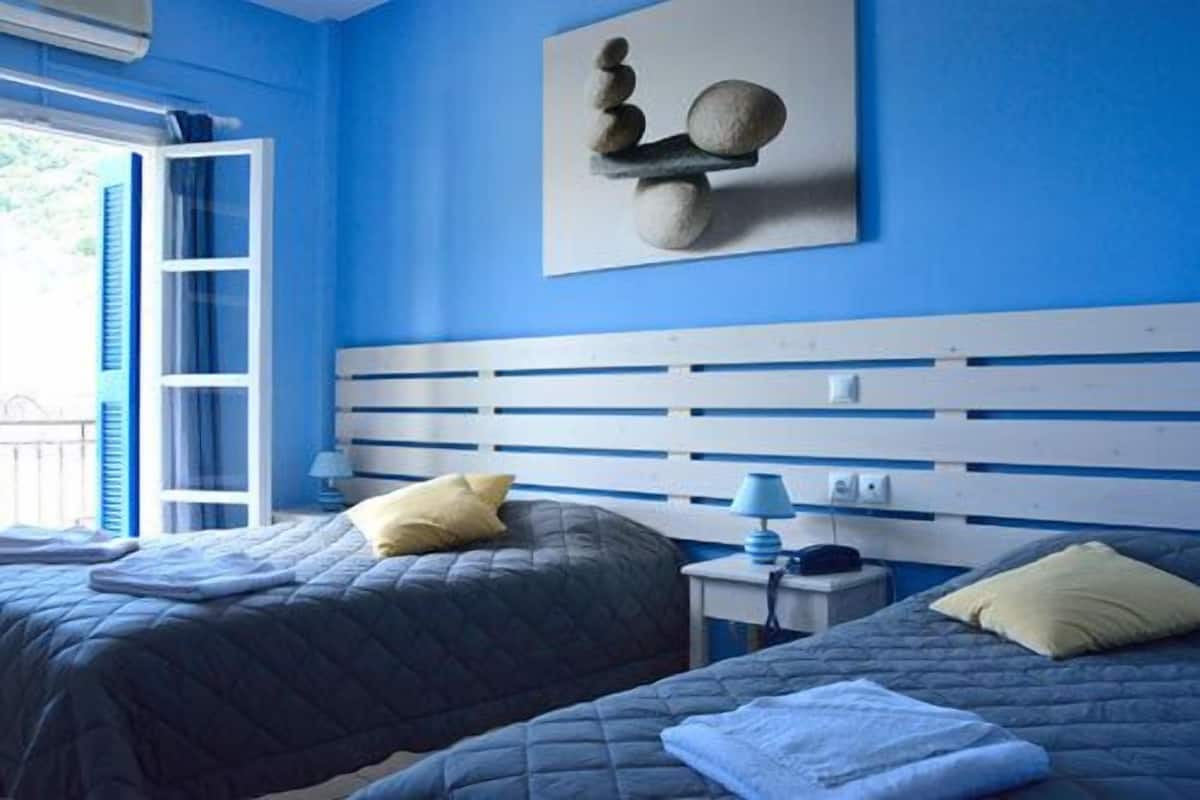 A room with two beds, a blue and white headboard, a wall-mounted artwork, and a window with blinds.