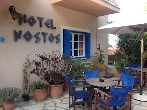 Un hôtel appelé « HOTEL NOSTOS », doté d’une terrasse et de plantes en pot.